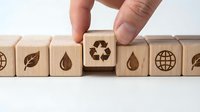 Hand selecting wooden cube with recycling symbol from row of eco-friendly icons representing sustainable business practices and environmental responsibility.