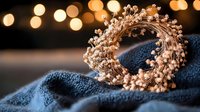 Delicate rose gold crown with tiny pearls and crystals on blue textile against blurred golden bokeh lights, romantic royal accessory for special occasions.