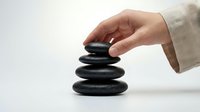 Hand placing dark smooth stone on balanced stack of four black zen rocks on white background, symbolizing harmony and mindfulness.