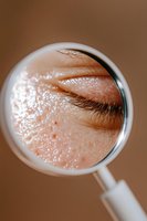 Close-up magnified view of skin texture and eyelashes through round magnifying glass showing pores, moisture and natural complexion details in macro photography.