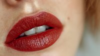 Close-up of woman's lips with glossy red lipstick showing natural skin texture and white teeth for beauty and cosmetics advertising campaigns.