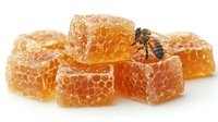 Fresh honeycomb pieces with natural golden honey and bee collecting nectar, macro photography on white background showing detailed hexagonal structure.