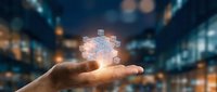 Businessman holding glowing digital puzzle piece above palm against blurred city lights, representing innovation, problem solving, and business strategy solutions.