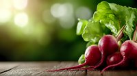 Fresh red radishes with green leaves on rustic wooden surface against blurred garden background with natural sunlight and bokeh effect.