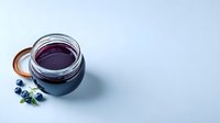 Fresh blueberry jam in glass jar with berries on blue background, homemade preserves for breakfast or dessert recipes.