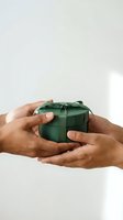 Hands holding small green gift box with ribbon bow for holidays, celebrations, and special occasions against neutral background.