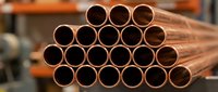 Stack of shiny copper pipes arranged in pyramid formation for plumbing, construction and industrial applications in warehouse setting.