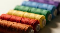 Colorful embroidery thread spools arranged in rainbow spectrum from orange to purple, sewing supplies for crafting and needlework projects on neutral background.