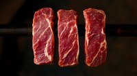 Fresh raw beef striploin steaks with marbling texture arranged in row on dark background, dramatic lighting highlights meat grain pattern and quality.