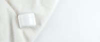 White cosmetic jar on cream knit fabric and light background, isolated for skincare product mockups and beauty packaging design.