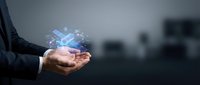 Businessman holding holographic digital technology icons in cupped hands representing innovation, connectivity and future business solutions in modern office.