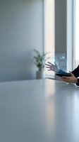 Businesswoman holding transparent tablet displaying digital interface with holographic data visualization, analytics charts and icons in modern office environment with natural light.