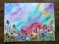 Watercolor meadow with colorful butterflies flying over wildflowers under a vibrant rainbow sky, painted on textured paper.