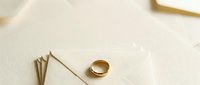 Young couple's golden wedding band resting on cream textured surface with decorative gold pins, symbolizing engagement, marriage commitment and romantic celebration moments.
