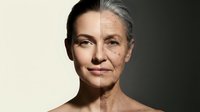 Split face portrait showing aging process from young to elderly woman with natural skin transformation and wrinkles development over time.