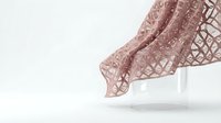 Flowing pink geometric patterned fabric with intricate lattice design draped elegantly against clean white background for textile and fashion projects.