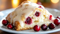Creamy white chocolate cranberry dessert slice on plate with fresh cranberries, topped with sweet glaze and cookie crust, macro food photography.