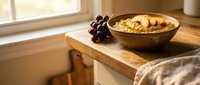 Wooden bowl filled with cereal and fresh grapes on windowsill, morning breakfast scene with natural light for food and lifestyle content.