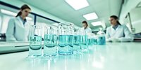 Laboratory glassware with test tubes and beakers on white surface in modern research facility with scientists working in background.