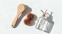 Wooden massage brush, cinnamon rolls and glass spray bottle arranged on white textured background for spa wellness and natural skincare routine.