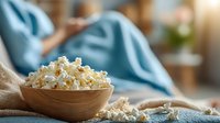 Fresh popped popcorn in wooden bowl on rustic table with cozy blanket background for snack and comfort food concepts.