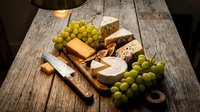 Assorted cheese and green grapes arranged on rustic wooden board with knife, ideal for food styling, culinary content, entertaining and gourmet themes.