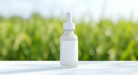 White dropper bottle with pipette for essential oils or serums on clean surface with blurred green nature background for natural skincare products.