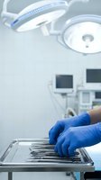 Surgeon hands in blue gloves arranging medical instruments on sterile tray in modern operating room with surgical lights and monitors.