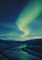 Mesmerizing aurora borealis dancing over winding river in snowy winter landscape at night, with starry sky and mountain silhouettes creating dramatic natural light show.