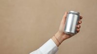 Hand holding silver aluminum beverage can against neutral beige background for product mockup and branding design applications.