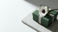 Elegant green gift box with cream ribbon and white anemone flower on textured surface, minimalist present wrapping for special occasions and celebrations.