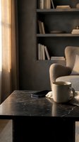 Cozy reading nook with steaming coffee mug on black marble table, notebook, comfortable armchair, and dark shelving unit with books in warm natural light for lifestyle and interior design projects.
