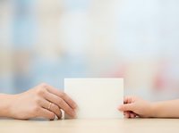 Two people exchanging blank white card at wooden table with soft blurred background, suitable for business communication, greeting cards, and corporate messaging designs.