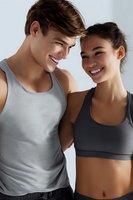 Young diverse athletic couple laughing together during workout. Caucasian man in tank top and Asian woman in sports bra share genuine moment at gym.