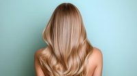 Young woman with long wavy blonde hair shown from behind against mint green background, demonstrating professional hair coloring and styling results for beauty salon advertising.