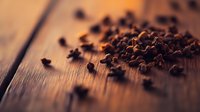 Aromatic cloves scattered on rustic wooden surface in warm lighting, creating moody atmosphere for culinary and spa concepts.