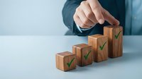Business professional arranging wooden blocks with green checkmarks in ascending order representing growth, success and achievement in corporate environment.