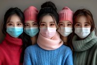 Group of young Asian women wearing protective face masks, winter knit hats and scarves in various colors standing close together during cold season.