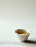 Minimalist white ceramic tea bowl with golden tea on light background, creating zen-like atmosphere and elegant composition for wellness and lifestyle designs.