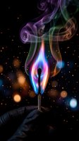 Colorful flame dancing above burning match with swirling smoke trails against dark background with bokeh lights for creative design projects.