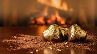 Gold nuggets on sandy ground with blurred fire flames in background, representing wealth, mining, and precious metals for finance and investment concepts.