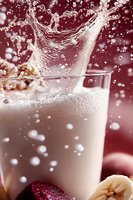 Dynamic splash of creamy milkshake with banana and strawberry pieces against burgundy background, capturing motion of liquid and droplets in macro photography.