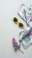 Stylish yellow sunglasses with floral silk scarf and fresh lilac flowers arranged on neutral background for fashion and lifestyle content.