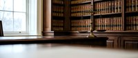 Classic law library interior with wooden bookshelves filled with legal volumes, natural window light illuminating polished desk surface for legal research.