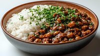 Homemade black bean stew served with white rice and fresh chopped parsley in ceramic bowl, traditional comfort food with rich sauce and herbs garnish.