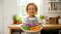 Young mixed-race girl with curly hair smiling while holding plate of fresh colorful vegetables in bright modern kitchen for healthy eating concept.