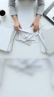 Woman in gray shirt organizing scattered documents and paperwork on white desk, overhead view for business workflow and office management concepts.