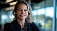 Professional blonde businesswoman smiling confidently in modern office environment with glass windows and contemporary lighting for corporate presentations.
