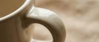 Close-up of smooth ceramic mug handle with warm beige tones and soft lighting creating elegant curves and shadows for kitchen and dining concepts.