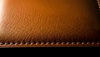 Brown leather texture with detailed stitching and grain pattern for luxury goods, fashion accessories, upholstery and premium material backgrounds.